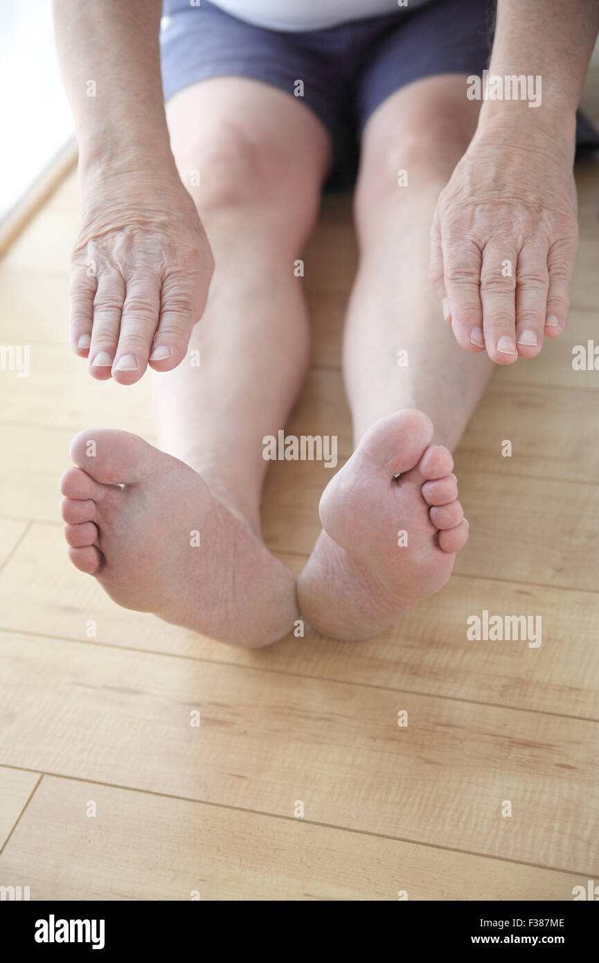 Senior man sits on floor and reaches for his toes, copy space included. Stock Photo