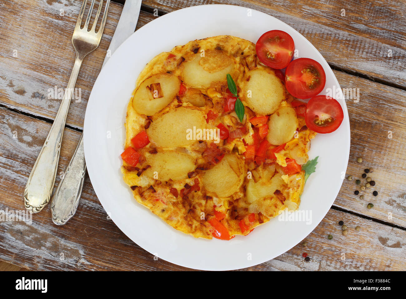 Omelette with potatoes, onions, red pepper and sweetcorn on white plate on rustic wooden surface Stock Photo