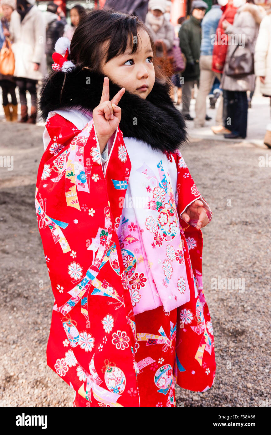 Sad faced Japanese child, girl, 4-5 years old. Wearing red and pink kimono  with black fur collar at new year festival, giving peace sign, eye-contact  Stock Photo - Alamy
