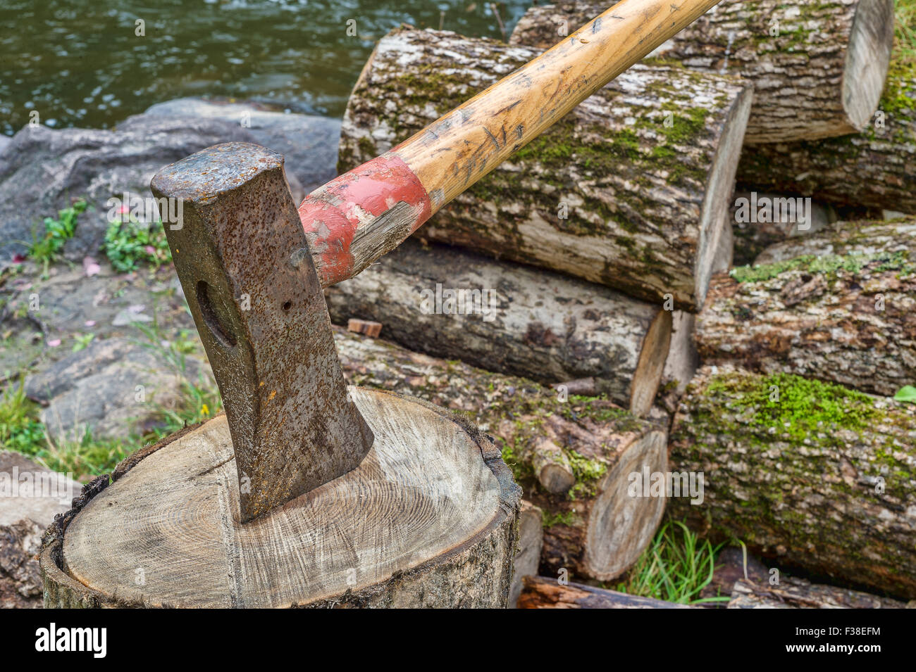 Axe on chopping block with a woodpile in the background Stock Photo