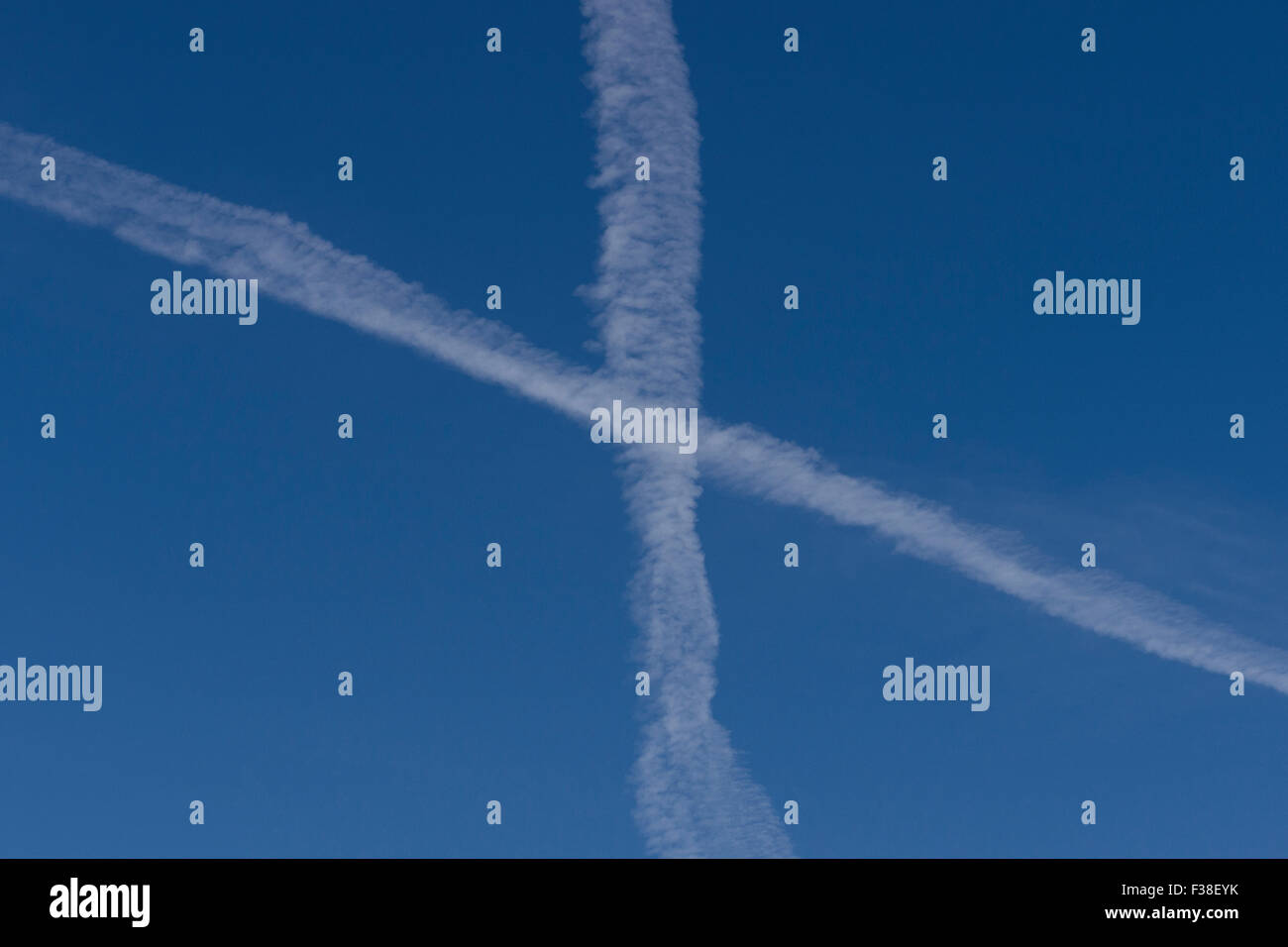 Two aircraft vapour trails crossing over in clear blue sky. Stock Photo