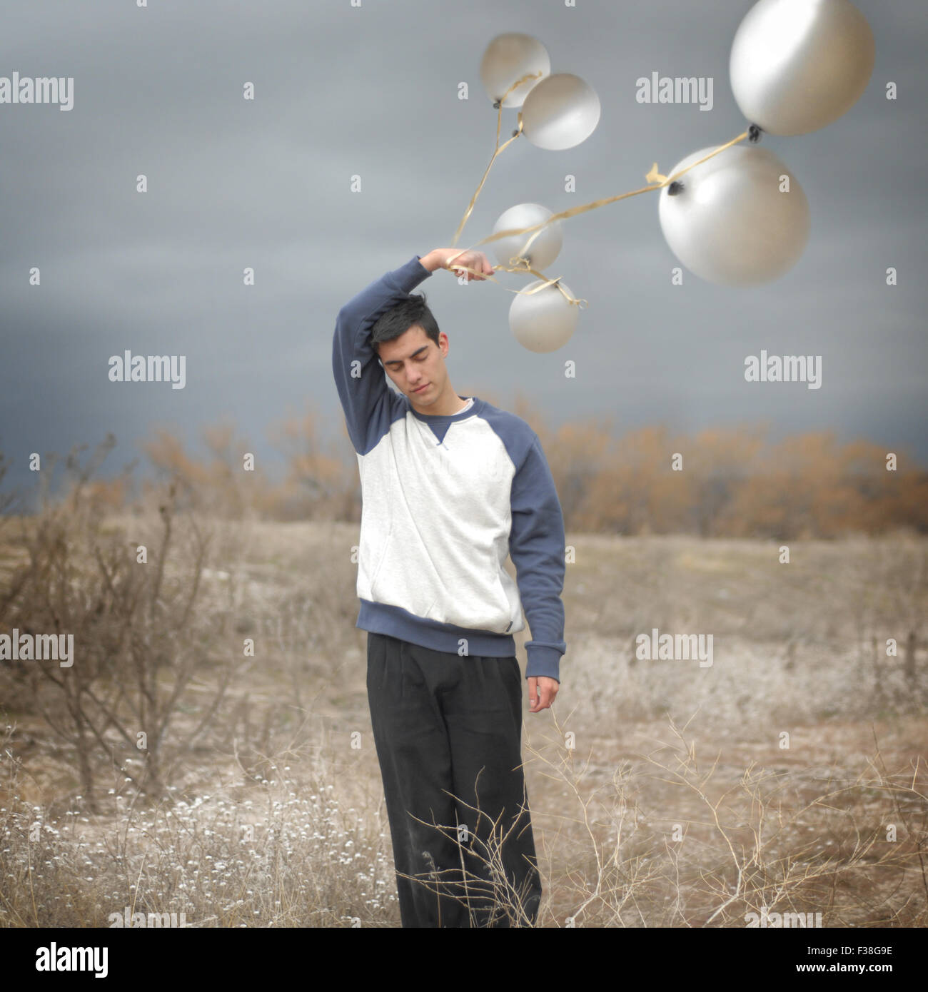 boy asleep holding silver balloons in the middle of the road windy day Stock Photo