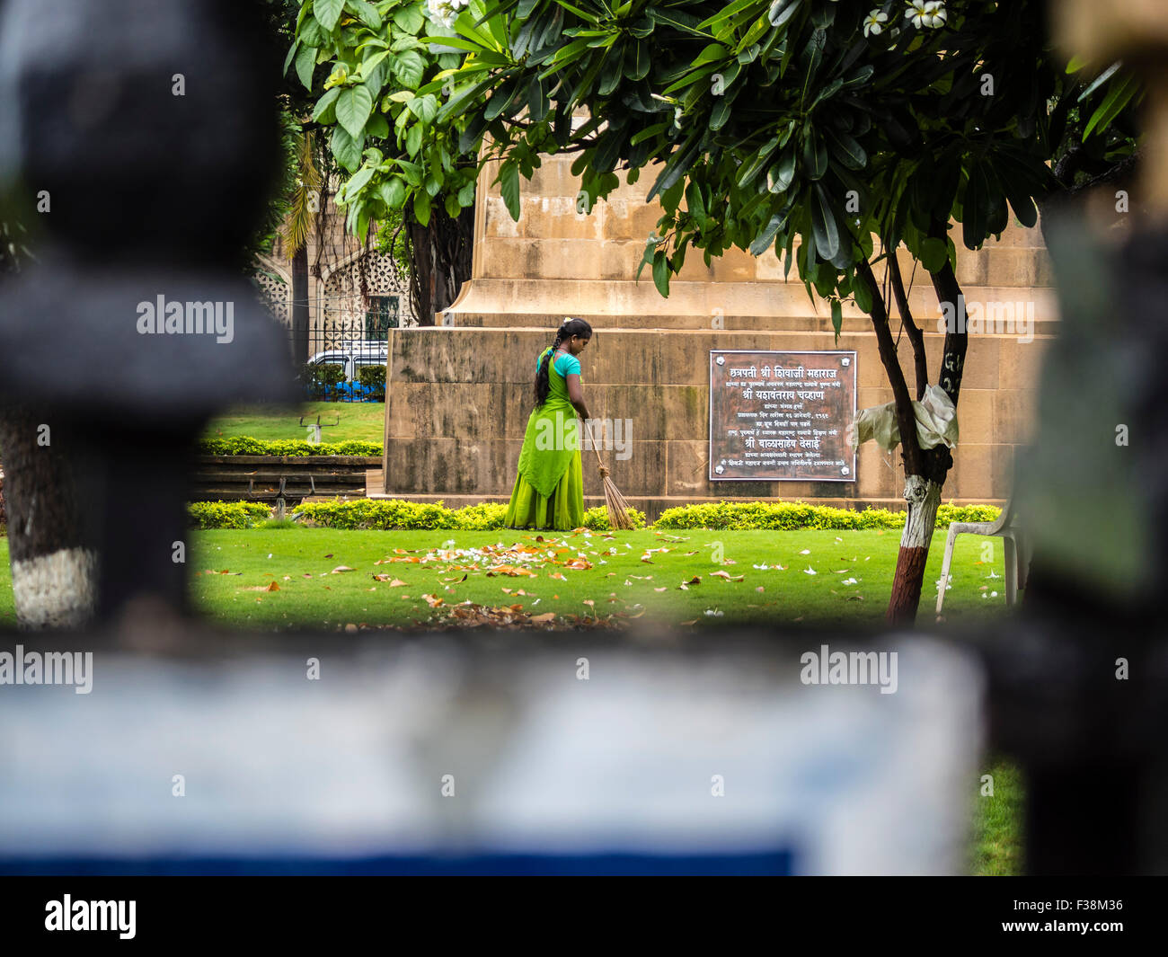Woman sweeping leaves, small park next to gateway of India, Mumbai, India Stock Photo