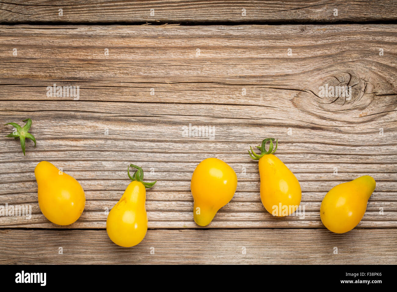 yellow pear tomato - a row of fruits on a grained weathered wood with a copy space Stock Photo