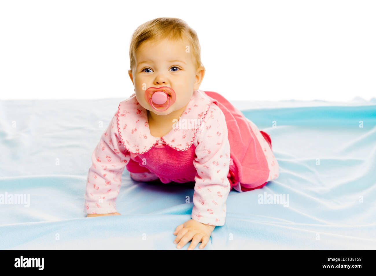Beautiful baby girl with pacifier crawling on the blue coverlet. Studio ...