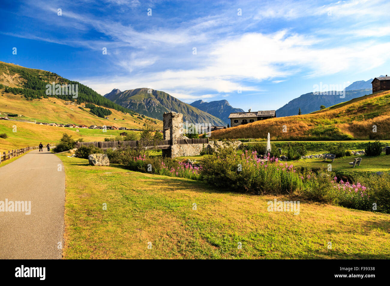 Picturesque landscape in Livigno, Lombardy, Italy with formal garden with an old stone building and benches, people on the road, Stock Photo