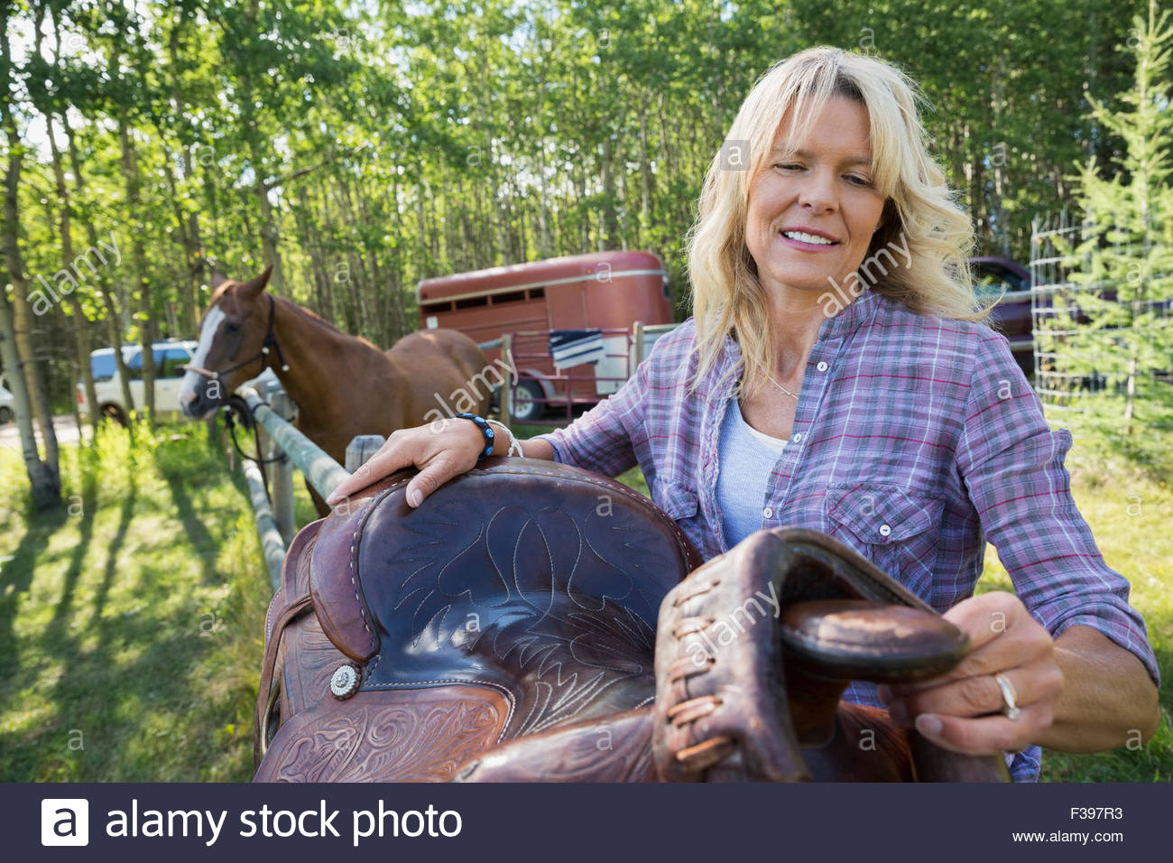 Woman adjusting saddle on fence near horse Stock Photo