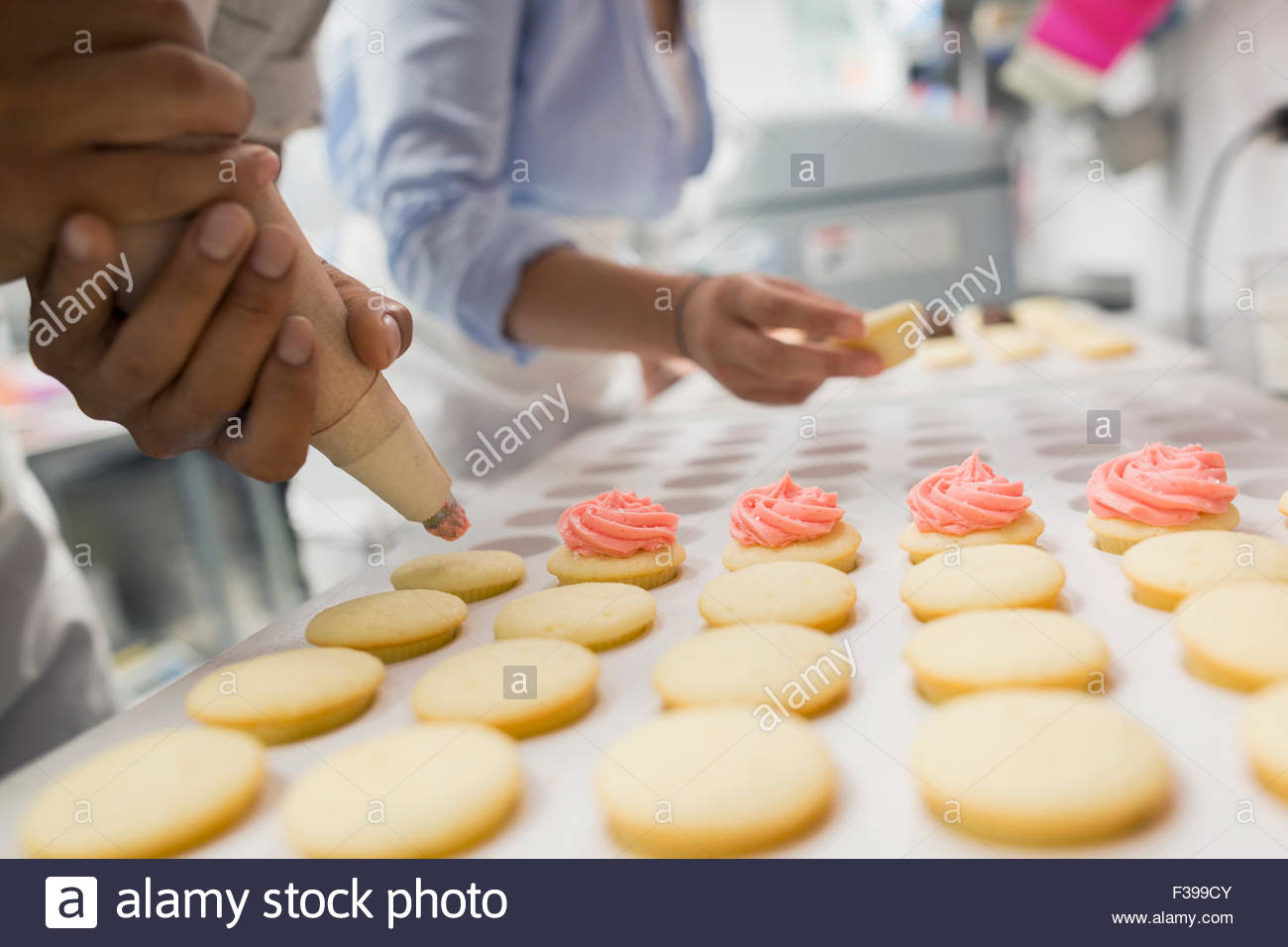 Close up pastry chef piping cookies pink icing Stock Photo