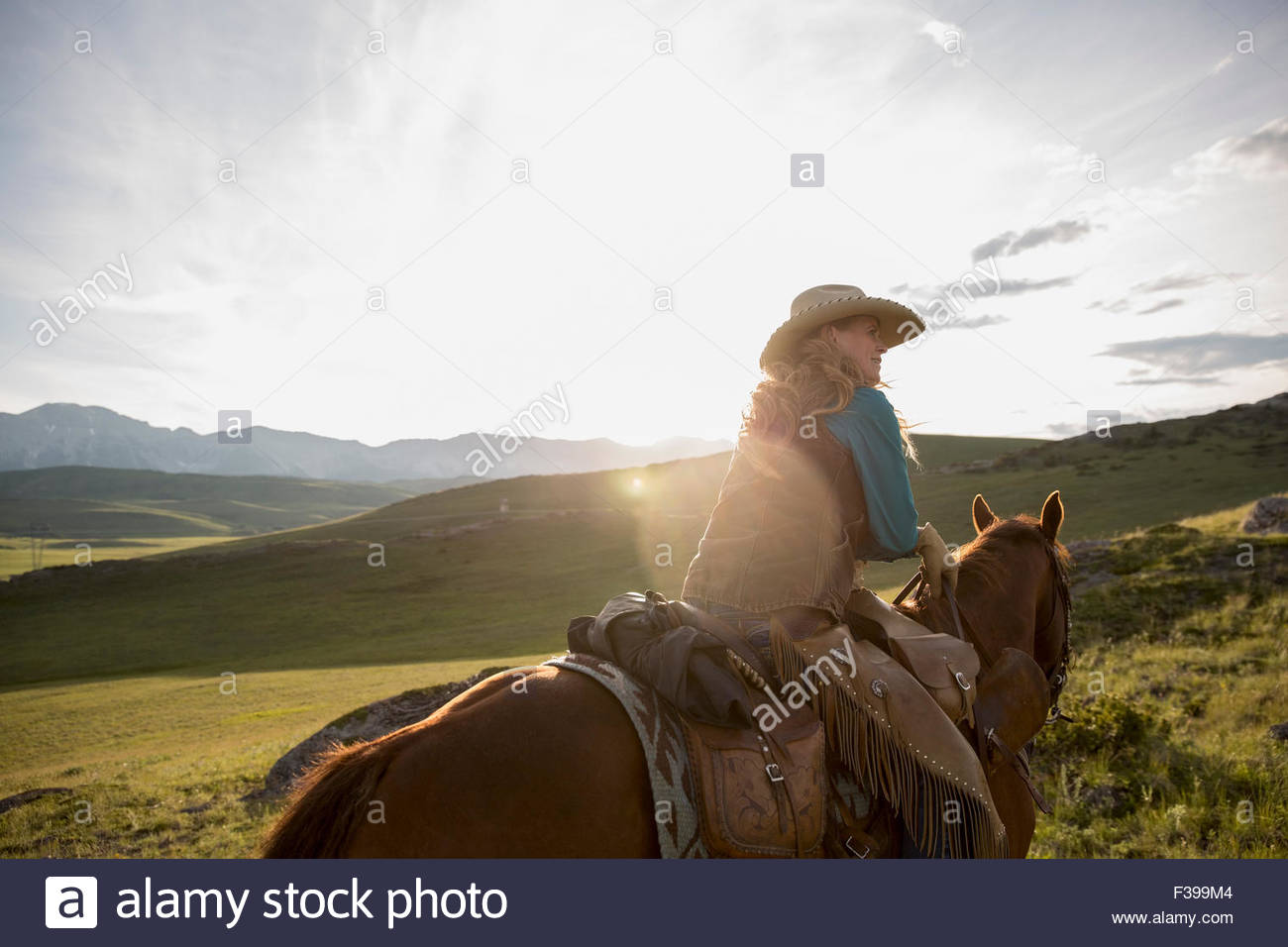 Female rancher horseback riding in remote sunny field Stock Photo