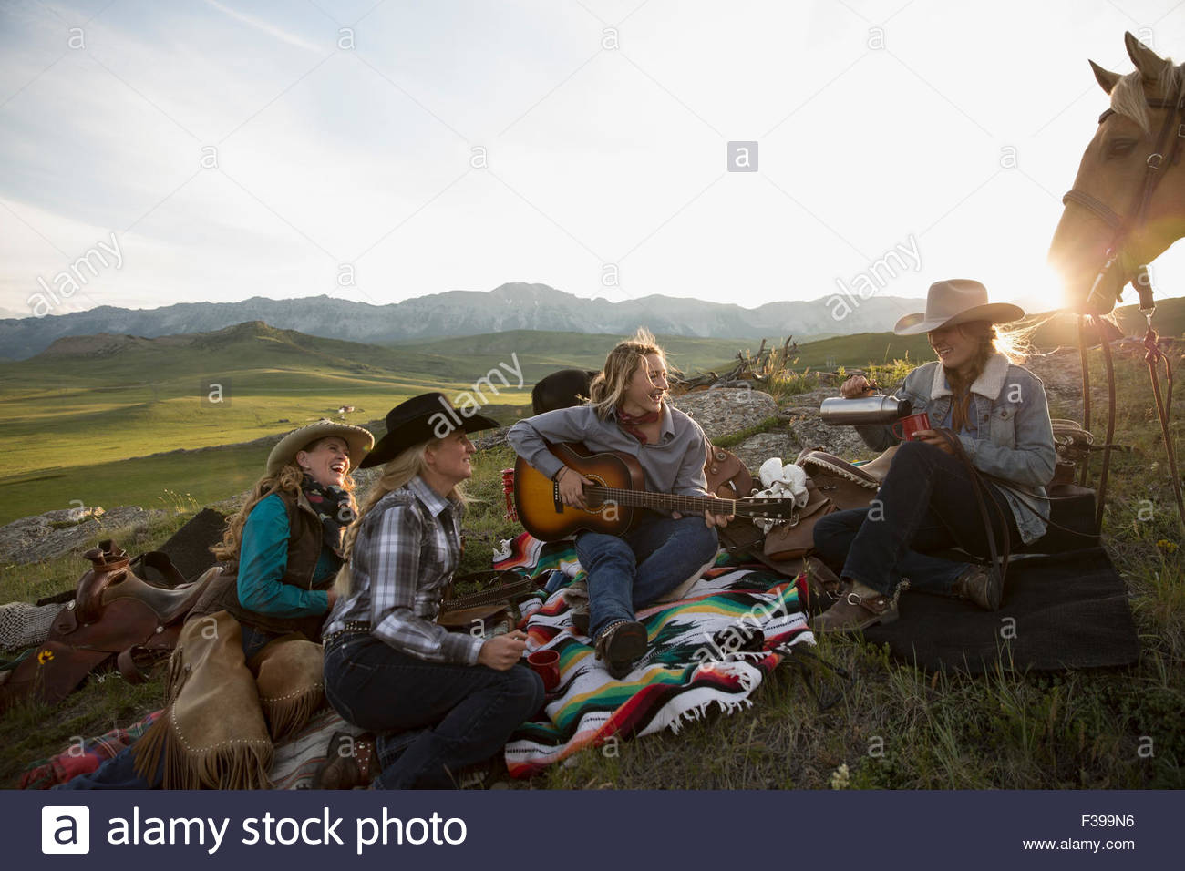 Female ranchers camping in remote field playing guitar Stock Photo
