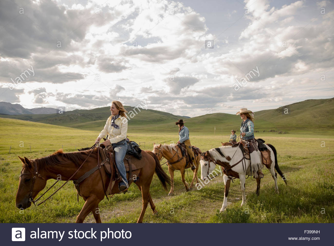 Female ranchers horseback riding in remote field Stock Photo
