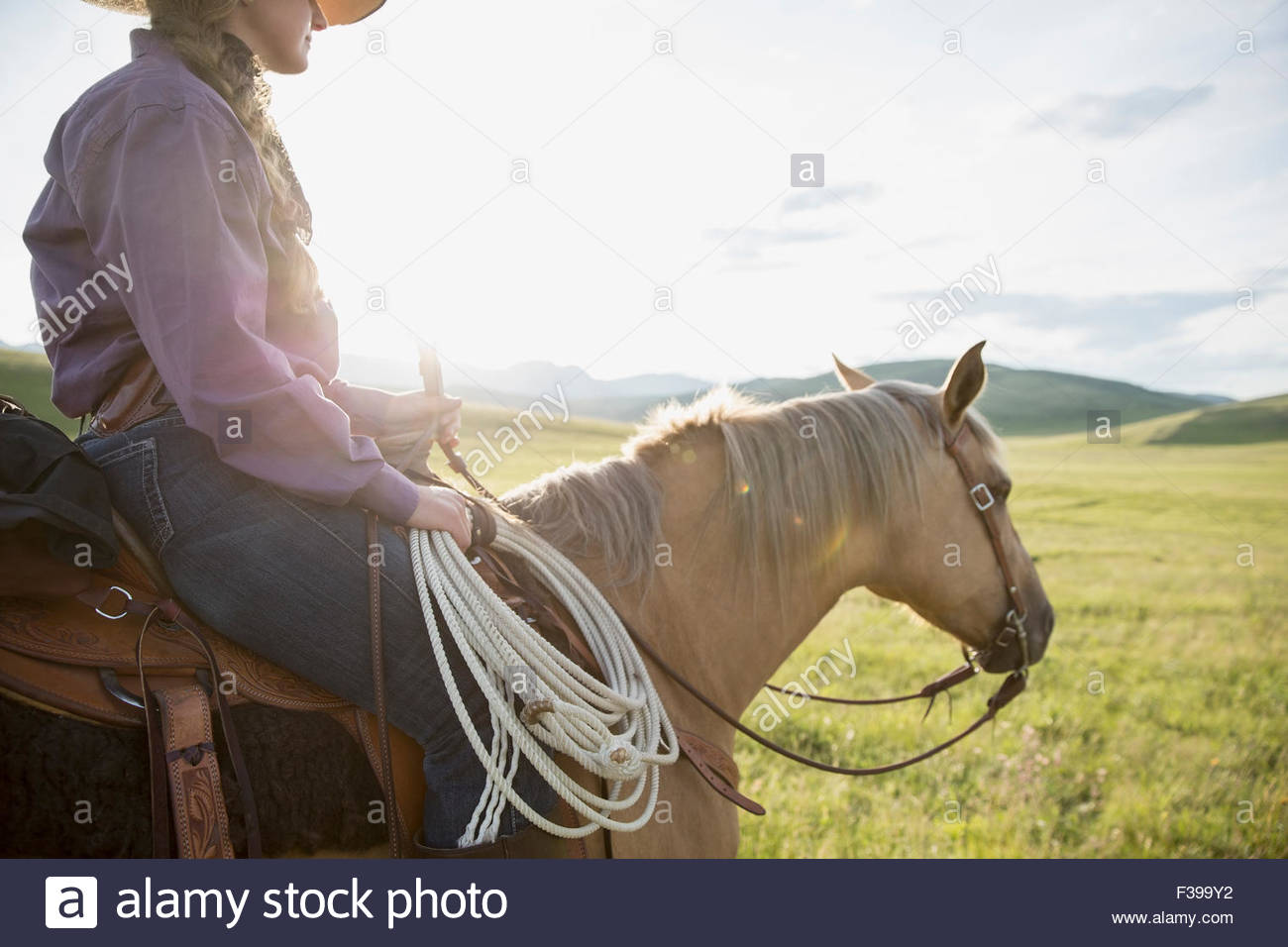 Female rancher horseback riding in sunny remote field Stock Photo