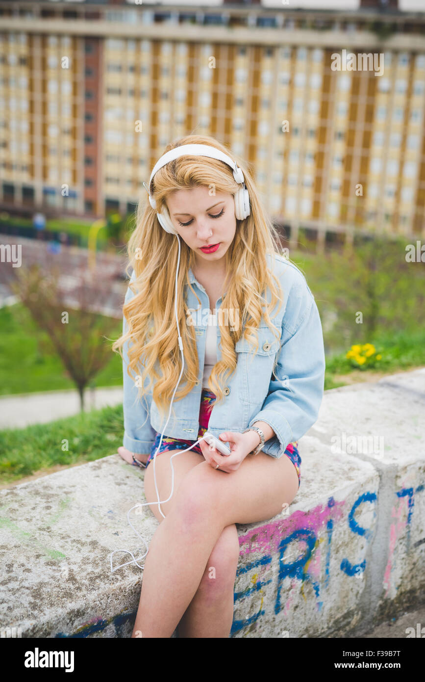 Young blonde caucasian girl listening music with headphones in the ...