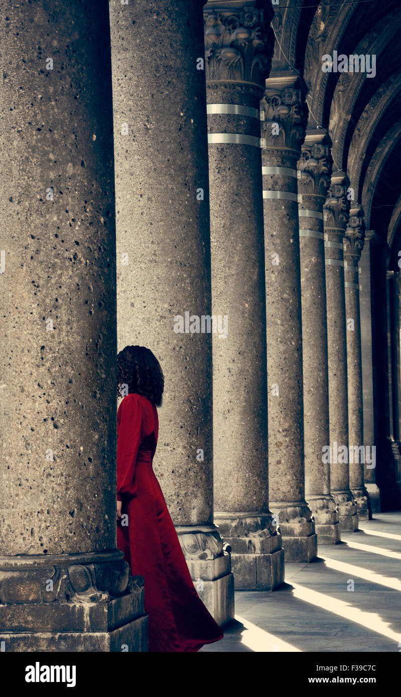 Mysterious woman in red dress behind column Stock Photo