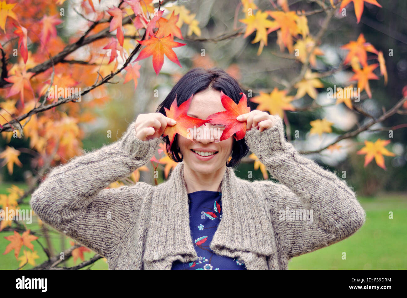 Smiling mid adult woman covering eyes with leaves autumn Stock Photo