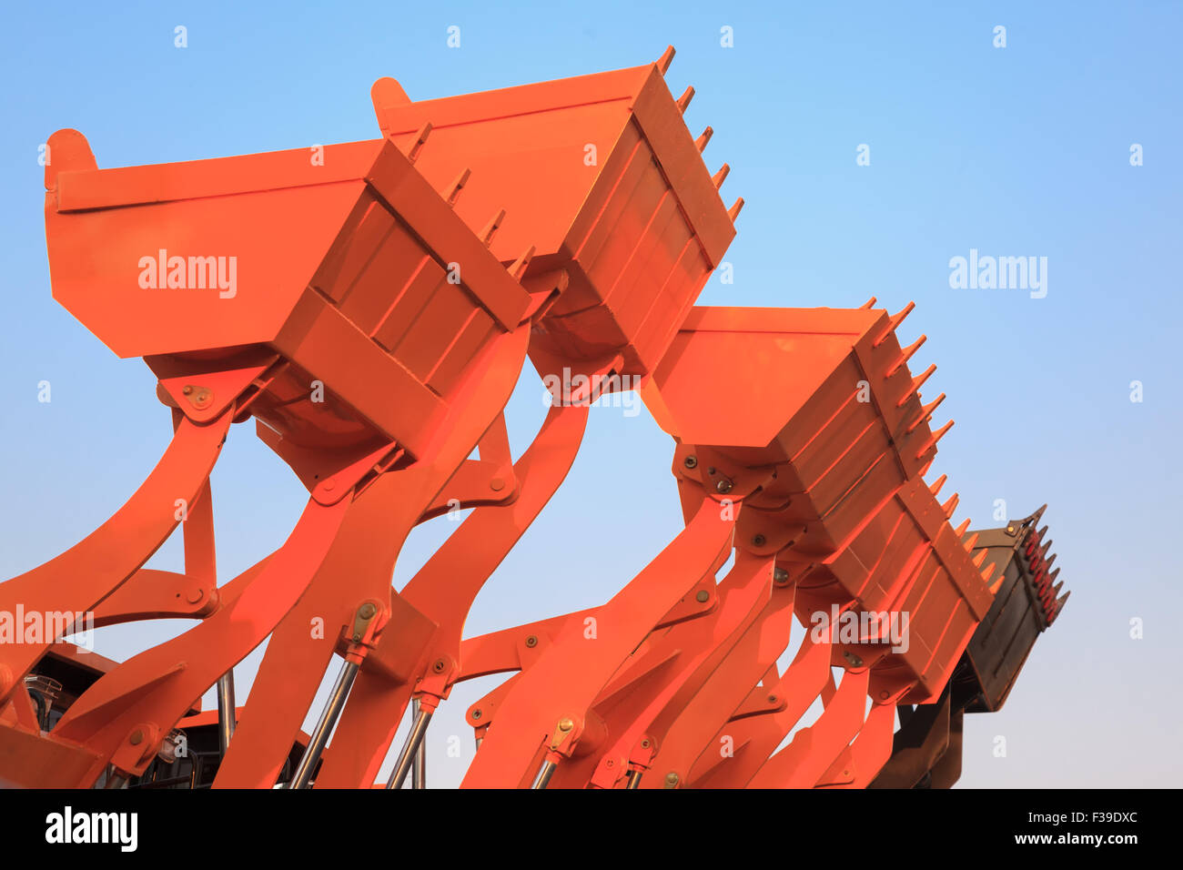 Part of modern yellow excavator machines,the buckets/shovels raised against blue sky in a construction site. Stock Photo