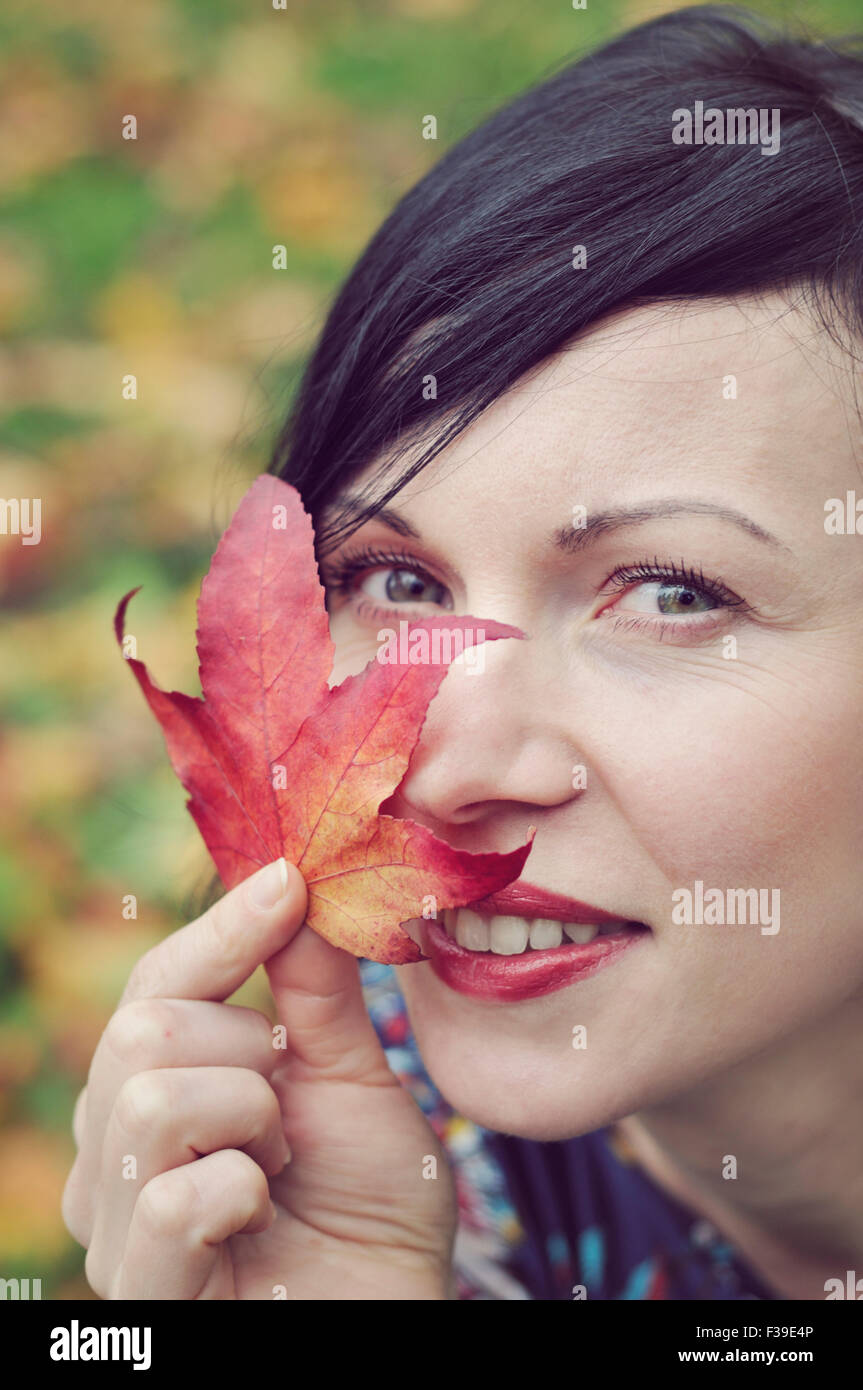 Smiling mid adult woman holding leaf close to her face Stock Photo - Alamy