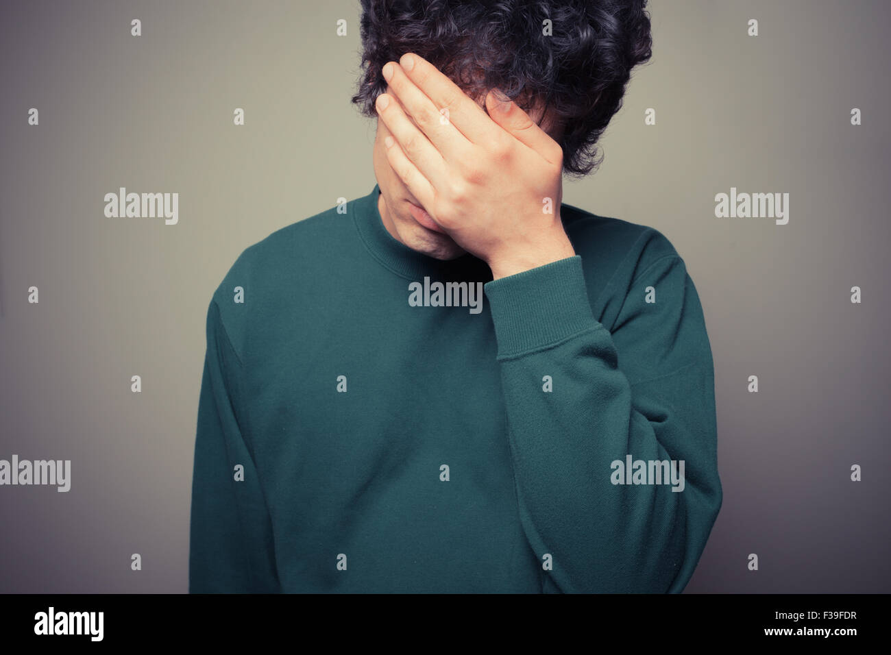 Young man is hiding his face in the palms of his hands Stock Photo