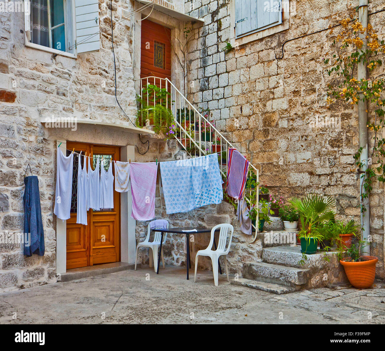 staircase full of plants and flowers leads to a Dalmatian house made of white stone blocks with laundry hanging behind Stock Photo