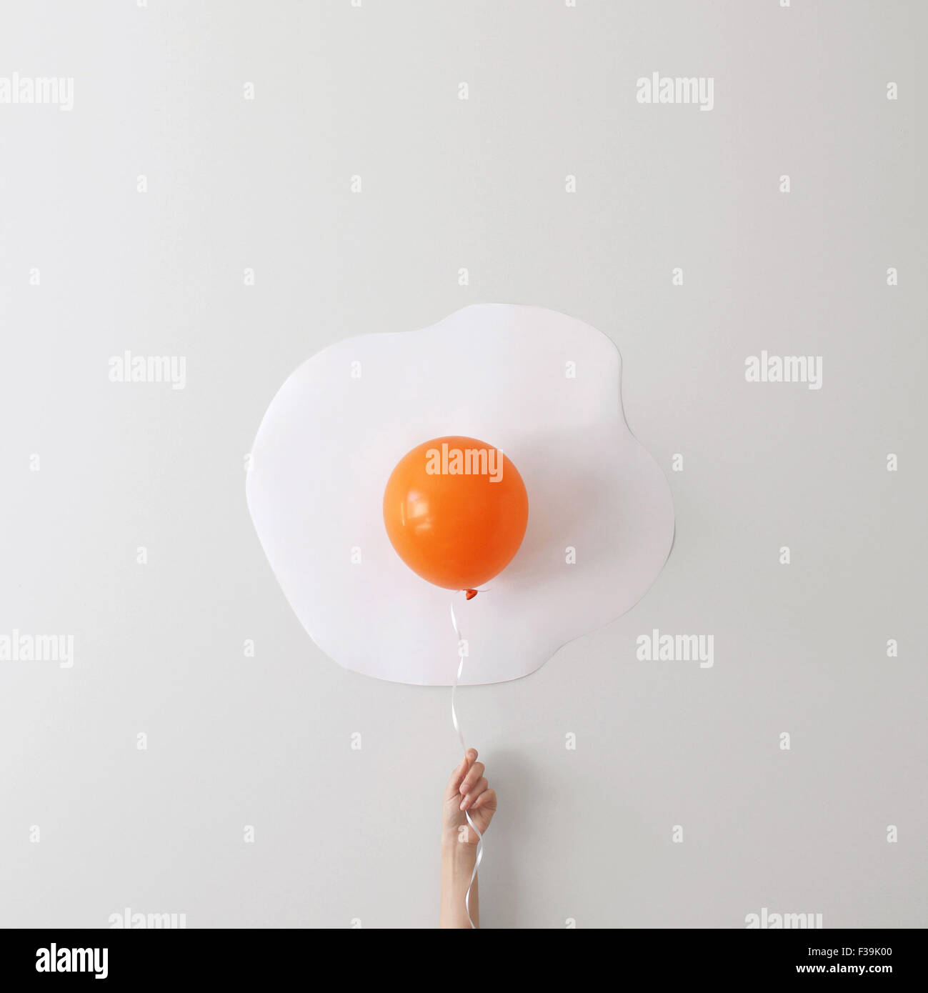 Woman holding a balloon against a wall creating a Conceptual fried egg Stock Photo
