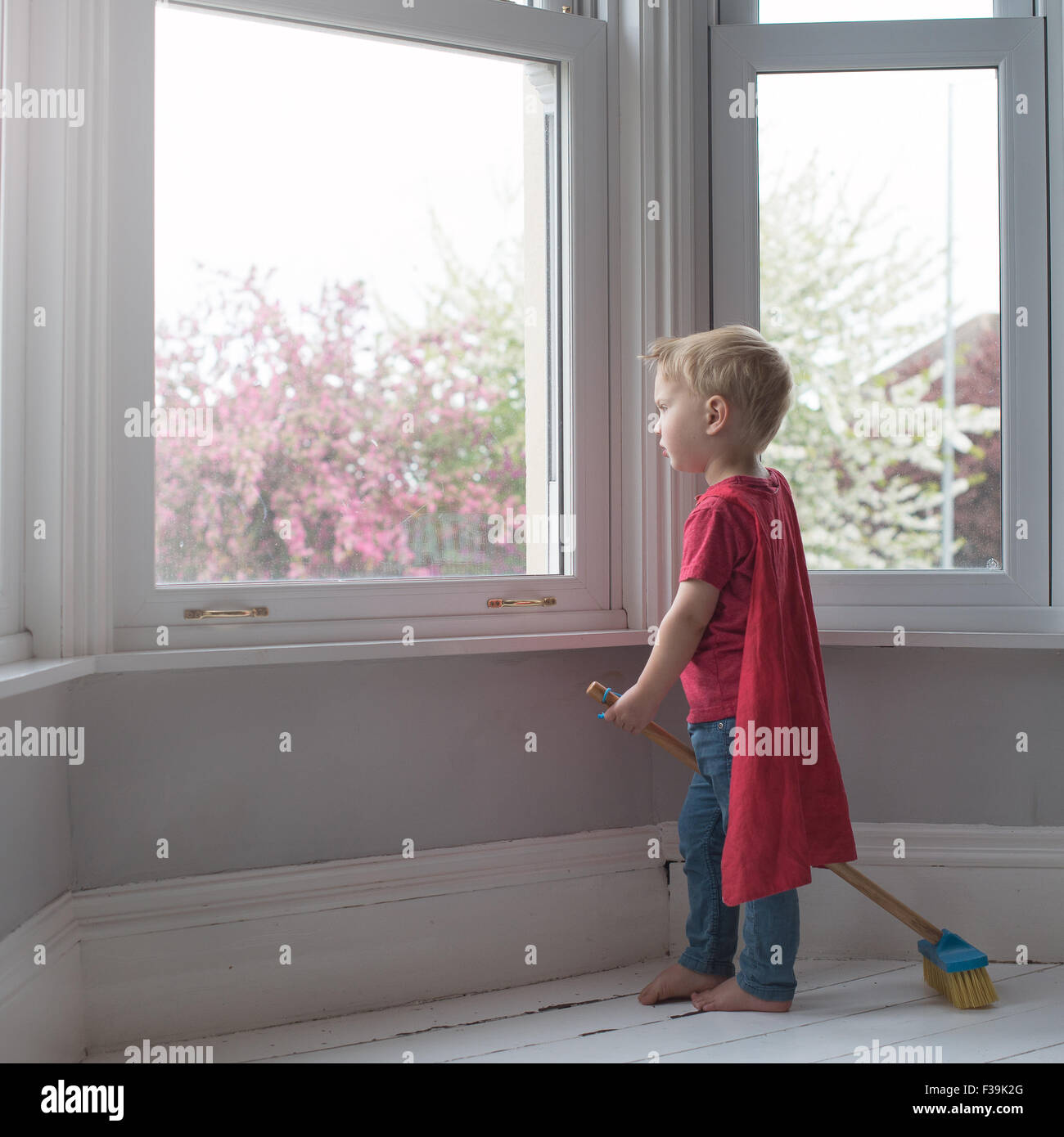 Boy dressed like superhero, looking through window Stock Photo