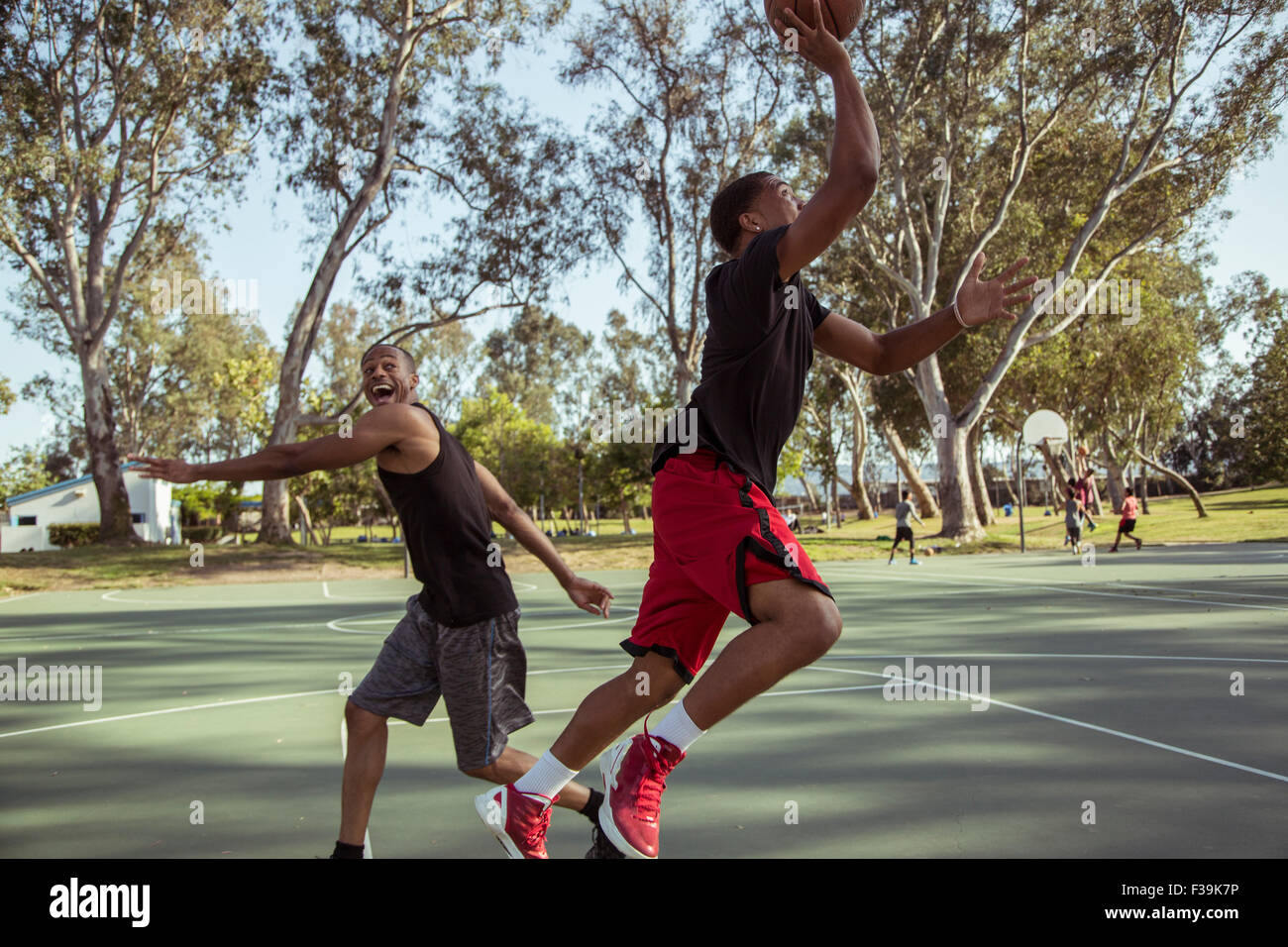 Two young men playing basketball, shooting hoops in the park at sunset Stock Photo