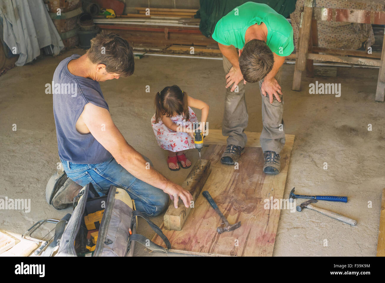 Girl helping two workmen drill a hole in a piece of  wood Stock Photo