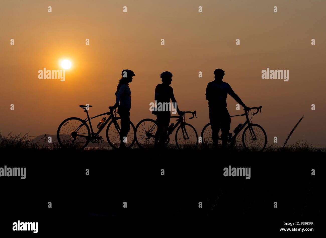 Silhouette of three cyclists at sunset Stock Photo