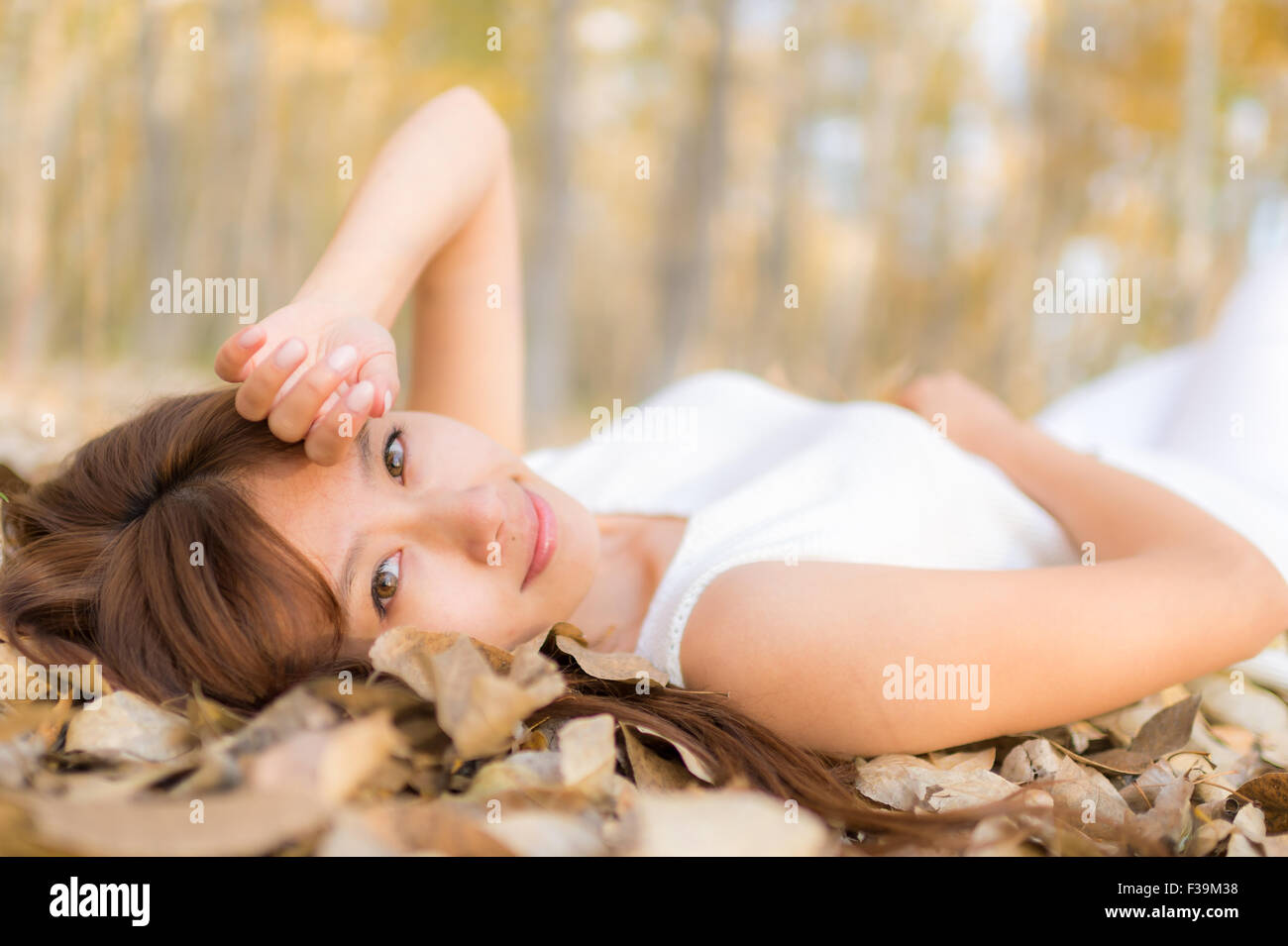 Portrait of a mid adult woman lying on a bed of autumn leaves in the forest Stock Photo
