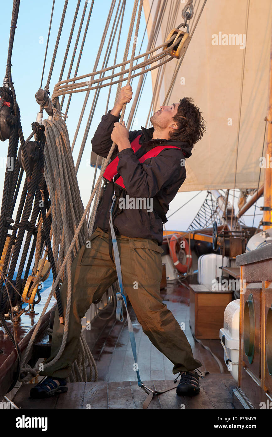 Young sailor on a ship's deck hoisting a sail Stock Photo