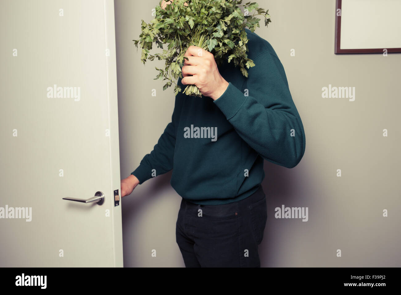 A young man with a big bunch of parsley in his hand is answering the door Stock Photo