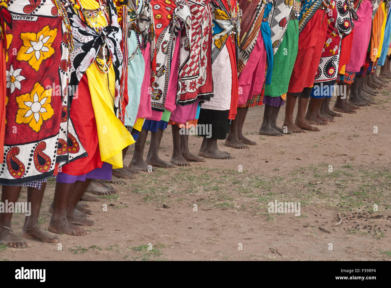 A line of barefoot Maasai Women wearing the traditional shawls called Kangas, in a village near the Masai Mara, East Africa Stock Photo