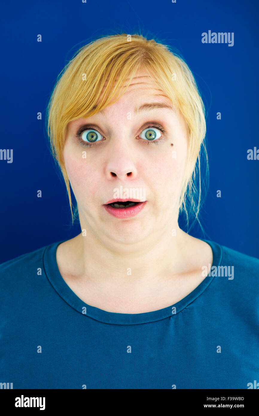 portrait of young blond woman looking surprised with blue background Stock Photo