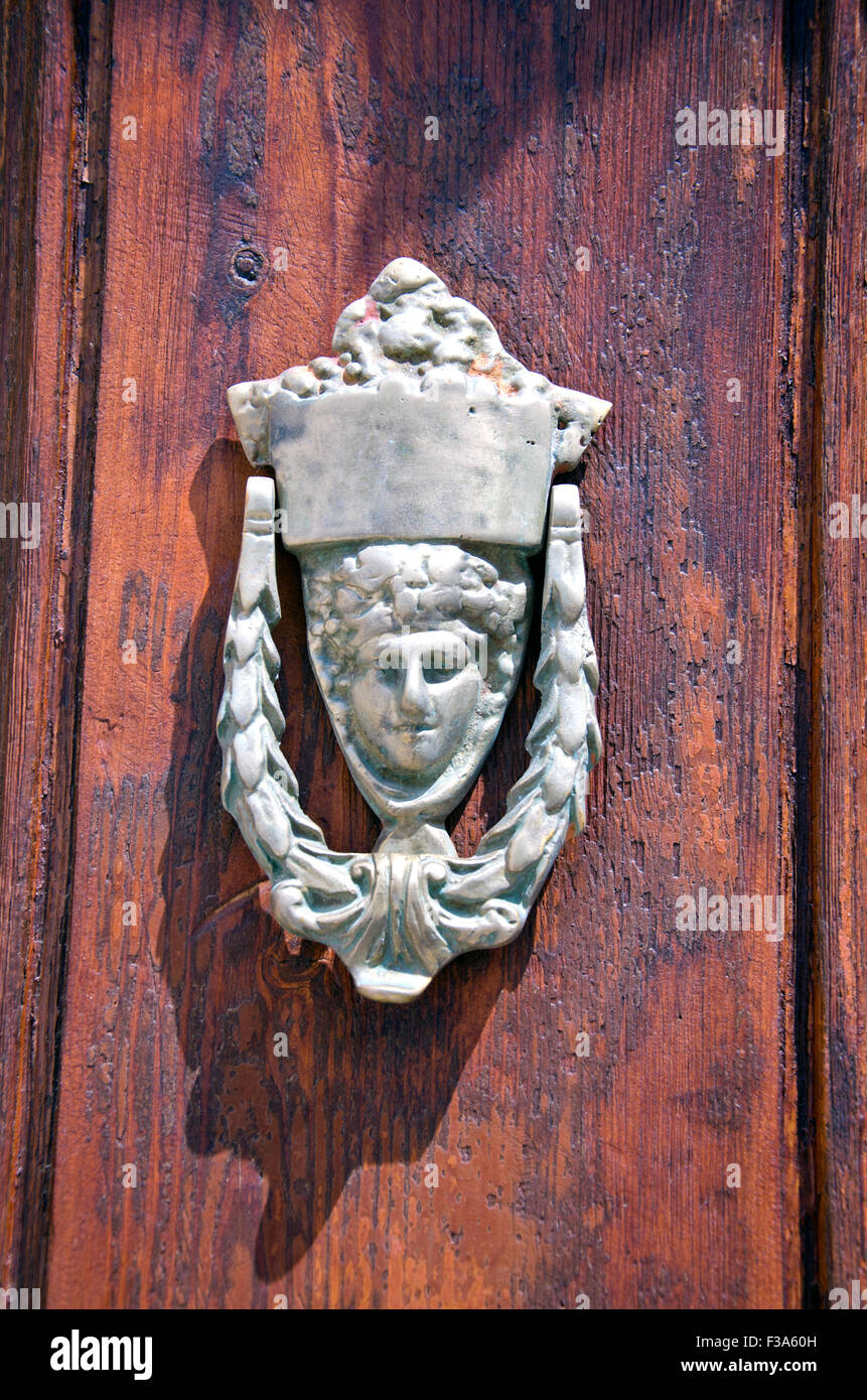 Antique door knocker in Greece with a face on old wooden door Stock Photo