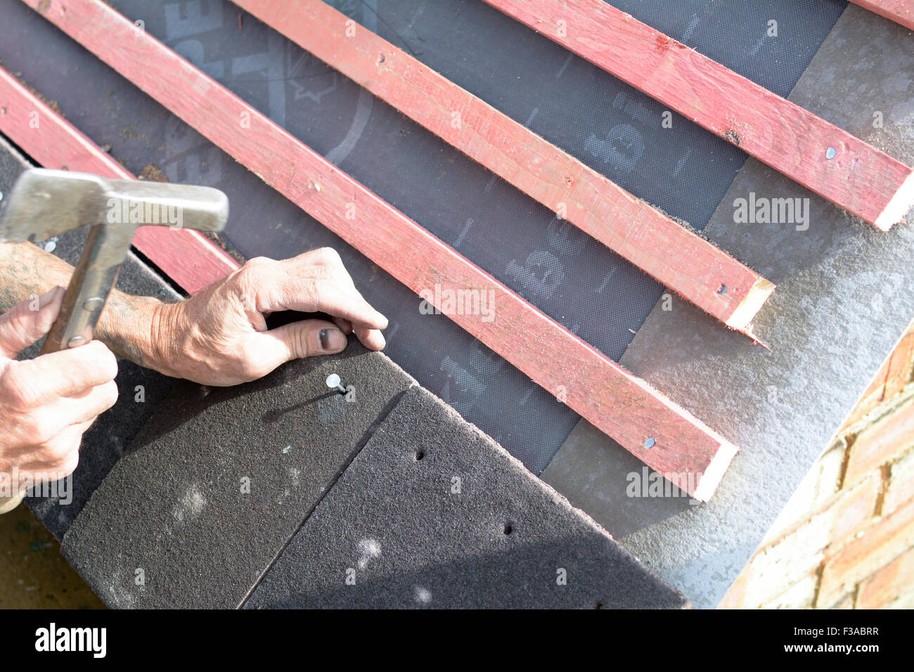A roofer using hammer to nail tiles to wooden roof battens in Bedford