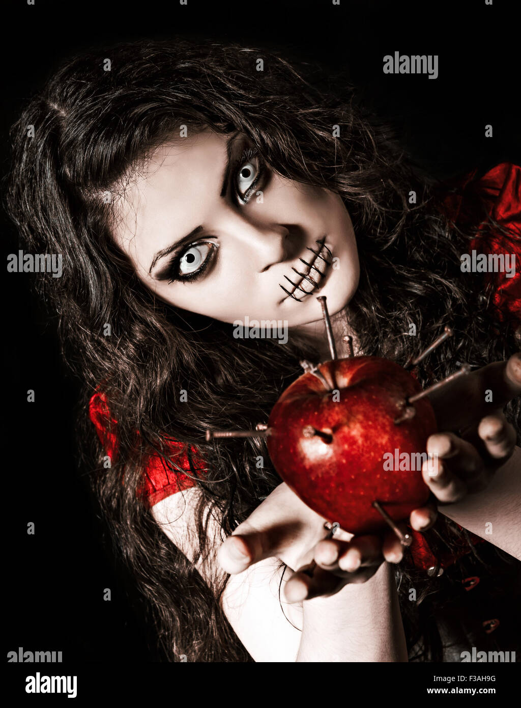 Horror shot: the strange scary girl with mouth sewn shut holds apple studded with nails Stock Photo