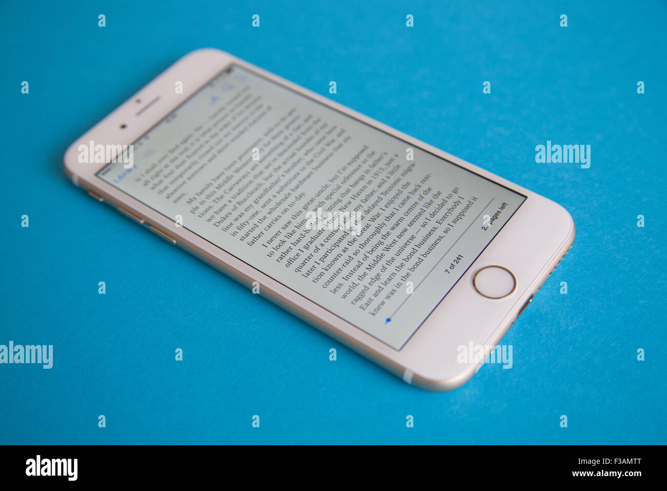Reading an ebook on a Gold and white Apple iPhone 6 againdt a blue background Stock Photo