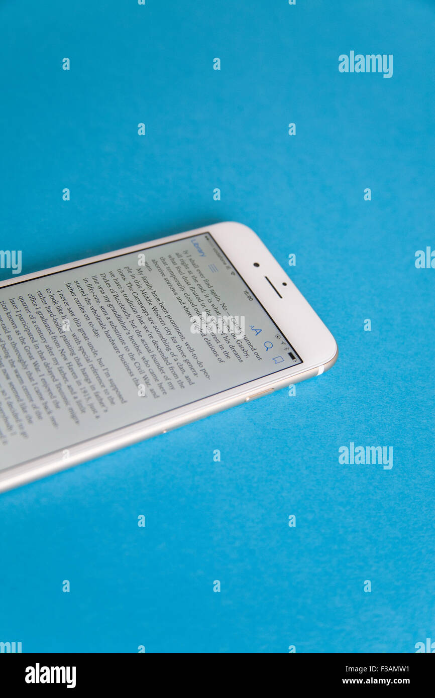 Reading an ebook on a Gold and white Apple iPhone 6 againdt a blue background Stock Photo