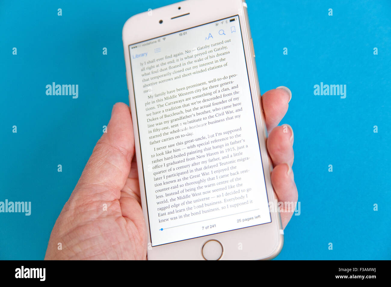 Reading an ebook on a Gold and white Apple iPhone 6 againdt a blue background Stock Photo