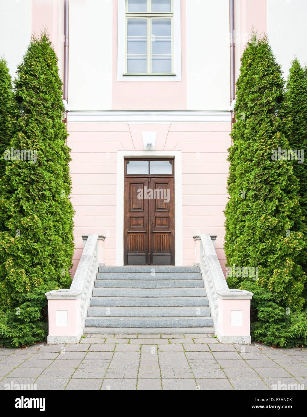 Stairway with tall green trees asides leading to a pink stone house with a dark brown wood door Stock Photo