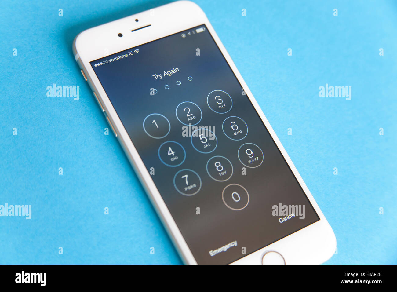 Gold and white Apple iPhone 6 with log in screen for password, against a blue background Stock Photo