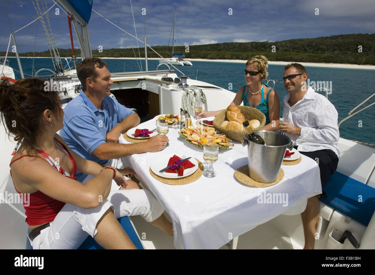 Mixed group having a relaxing lunch on board anchored yacht Whitsunday Islands Queensland, Australia Stock Photo