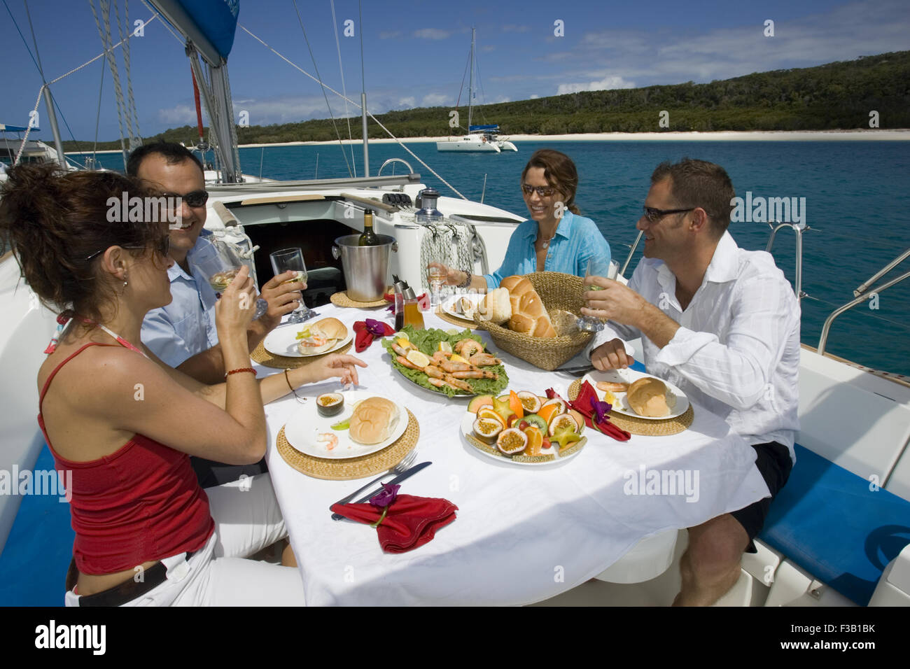 Mixed group of people having a relaxing lunch on board anchored yacht Whitehaven Bay Whitsunday Stock Photo