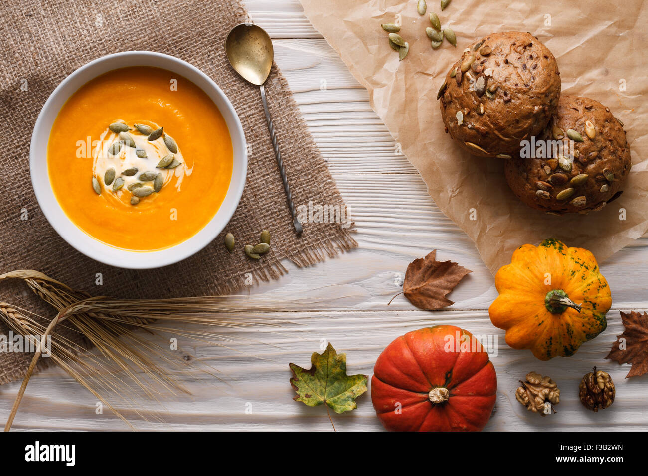 Traditional pumpkin soup with seeds and fresh just baked rye bans on a white wooden background. Stock Photo