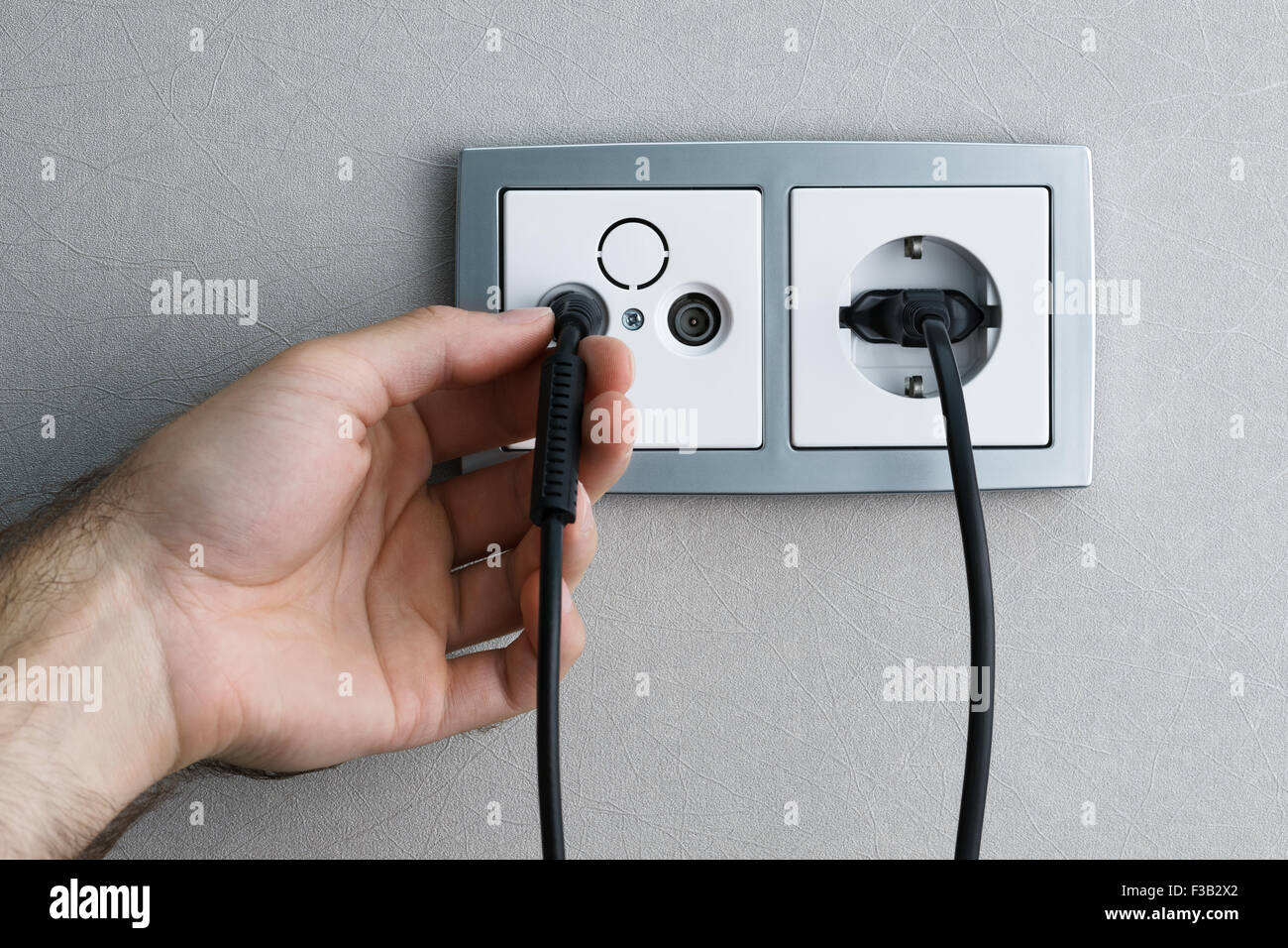 A man hand plugging antenna cable to the TV outlet Stock Photo