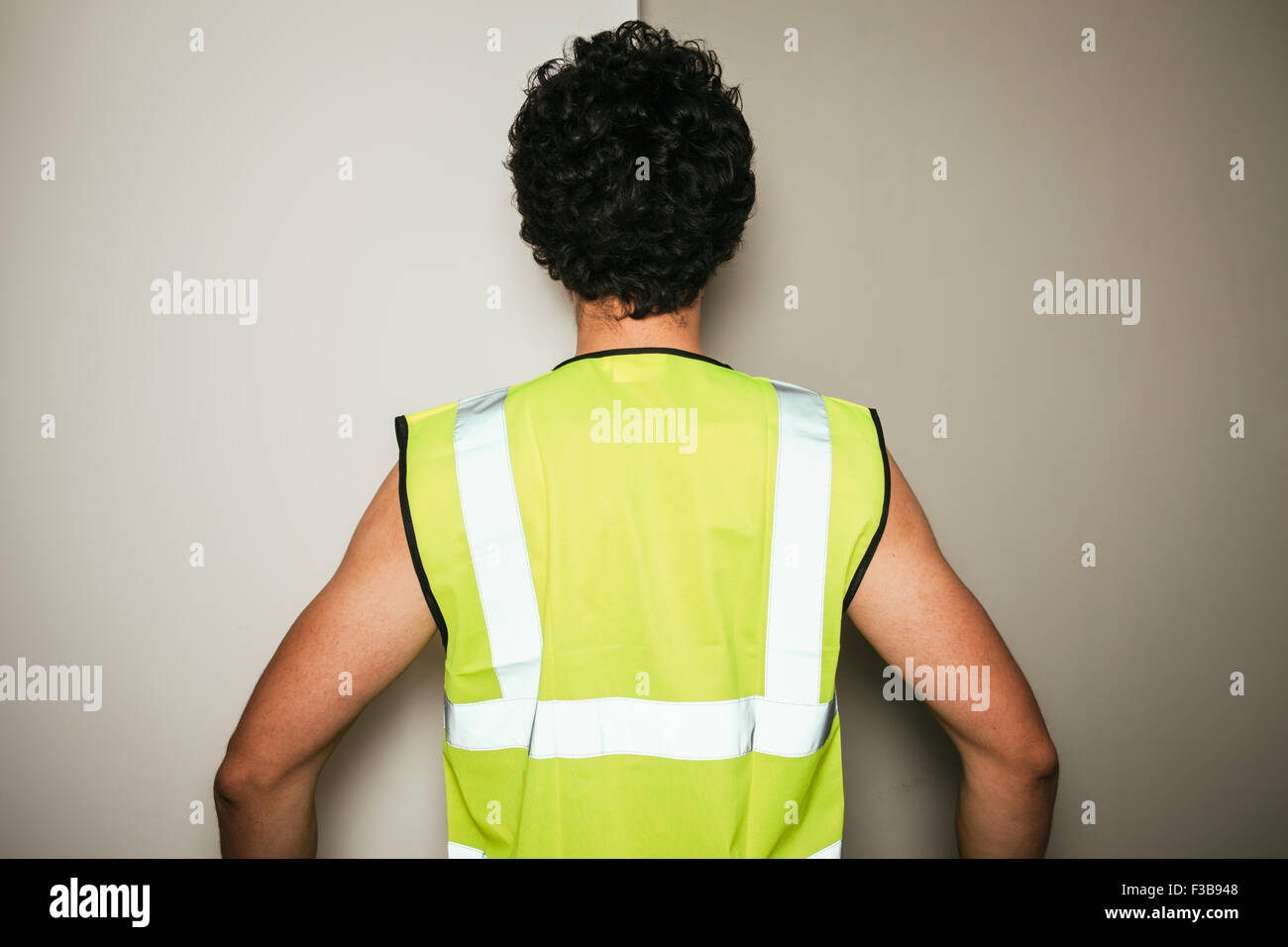 Rear view of a builder in a high visibility vest against a green and white background Stock Photo