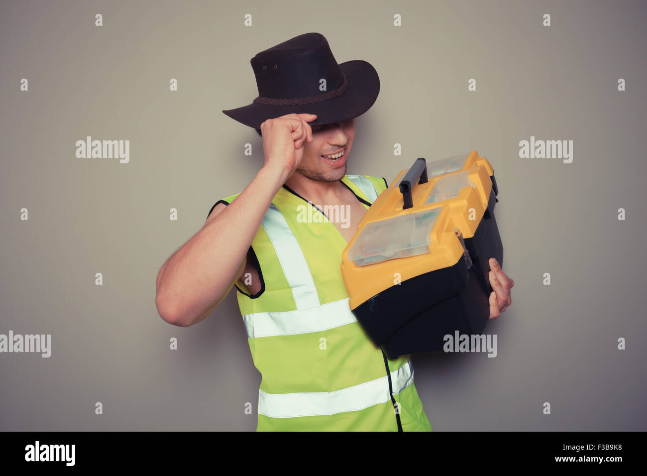 A cowboy builder with a big tool box is pulling silly faces and