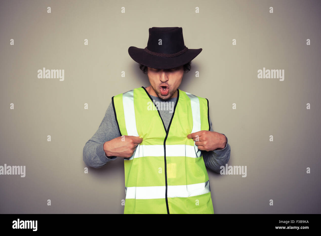A cheeky cowboy builder is wearing a high visibility vest and twisting his nipples Stock Photo