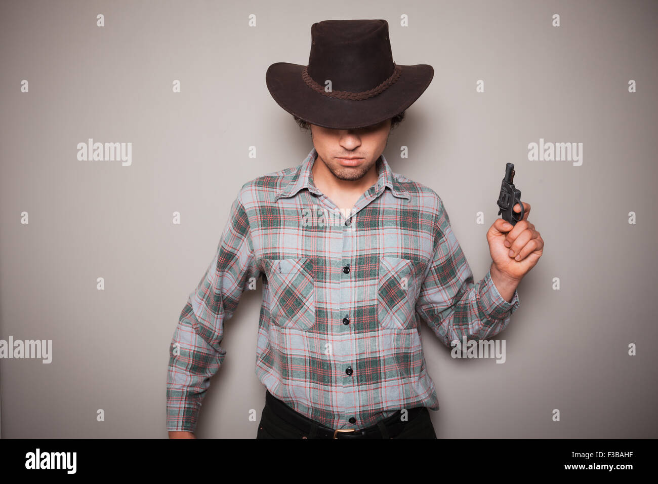 A young man wearing a cowboy hat and a plaid shirt is holding a revolver Stock Photo