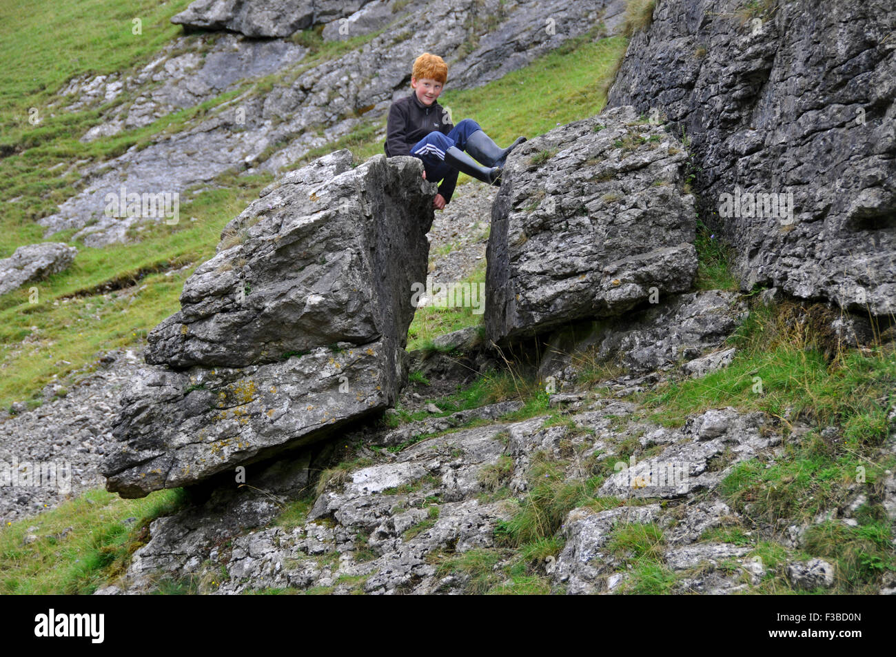Red-haired boy having fun on split (maybe by frost) limestone rocks in the Dovedale, Peak District, Derbyshire, England Stock Photo
